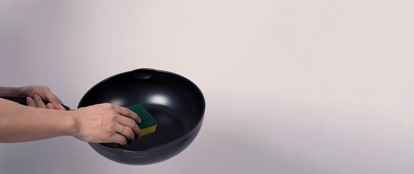 Asian man in grey color T shirt cleaning the non stick pan with handy dishwashing sponge which yellow color on the soft side and green on hard side for hygiene after cook and white background studio shot