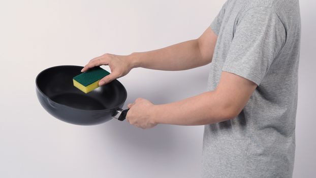 Asian man in grey color T shirt cleaning the non stick pan with handy dishwashing sponge which yellow color on the soft side and green on hard side for hygiene after cook and white background studio shot