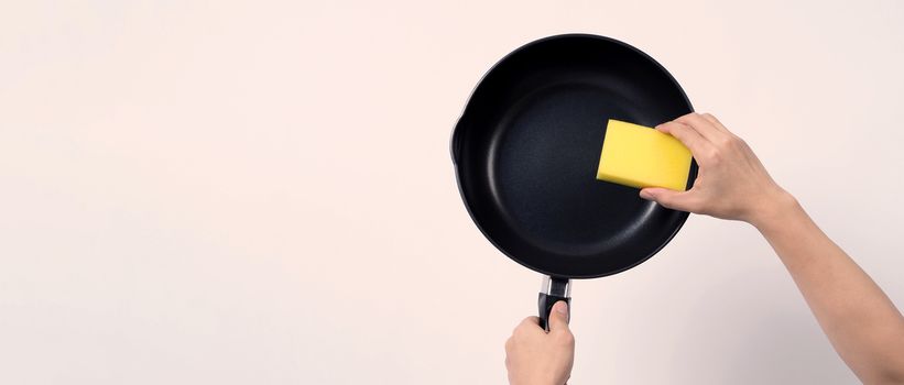 Asian man in grey color T shirt cleaning the non stick pan with handy dishwashing sponge which yellow color on the soft side and green on hard side for hygiene after cook and white background studio shot