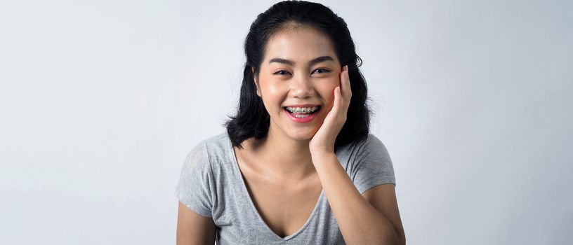 Asian teen facial with braces and smiling to camera to show dental orthodonic teeth which include professional metal wire material from orthodontist. studio shot white background.