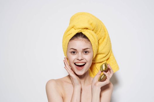 Cheerful woman with a yellow towel on her head bare shoulders of kiwi in her hands. High quality photo