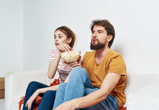friends man and woman with popcorn in a plate indoors on sofa interior. High quality photo