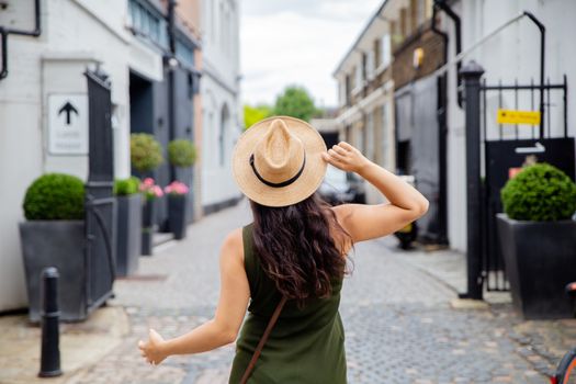 Landscape View of a Joyful Woman in Green Dress From Behind Poses while holding her hat, in front of an Alley Entrance from London, UK