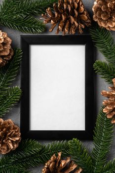 Christmas composition with empty picture frame. Golden ornament, pine cones and fir needles decorations. Mock up greetings card template