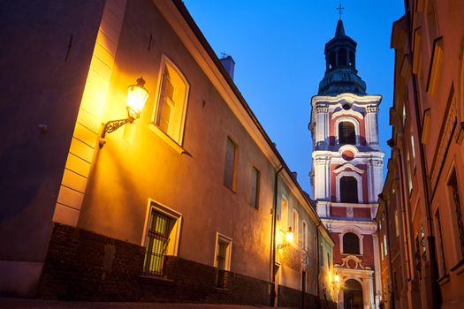 narrow street and belfry of the baroque historic church at night in Poznan