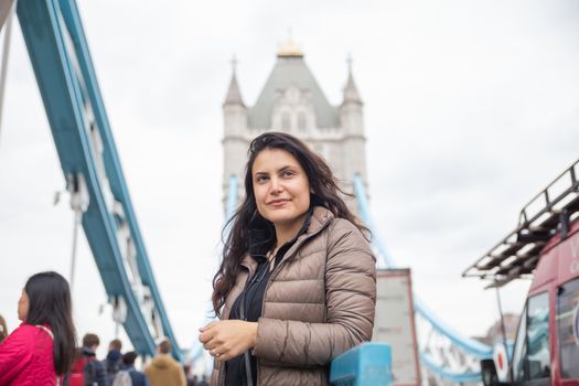 Picture of a long haired woman with a blurry Tower Bridge and a cloudy sky as background