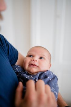 Portrait style picture of a baby beign hold in the arms of her father with a blurry white door as background