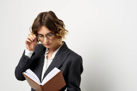 Woman at work with book in hand light background classic suit glasses head. High quality photo
