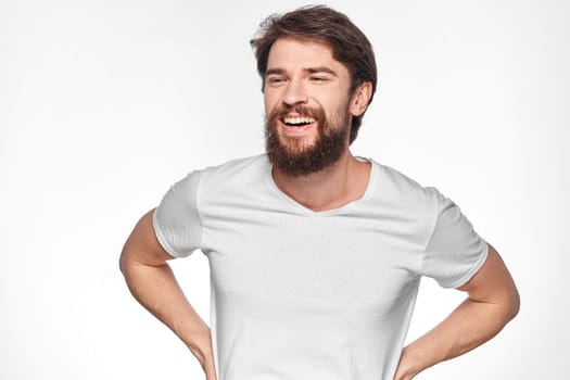 cheerful bearded man in a white t-shirt emotions gestures with his hands light background studio. High quality photo