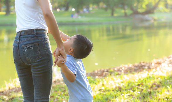 Asian mother or parent and son holding hand with love together in summer outside in the park, mom take care kid holding palm with affection, child have a trust for mother, family concept.