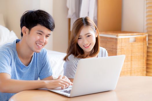 Asian young couple using laptop computer think and searching internet together, man and woman casual smiling work at home with happy and relax, communication and business concept.