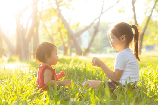 Beautiful young asian kid sitting playing in summer in the park with enjoy and cheerful on green grass, children activity with relax and happiness together on meadow, family and holiday concept.