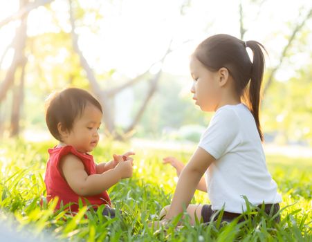 Beautiful young asian kid sitting playing in summer in the park with enjoy and cheerful on green grass, children activity with relax and happiness together on meadow, family and holiday concept.