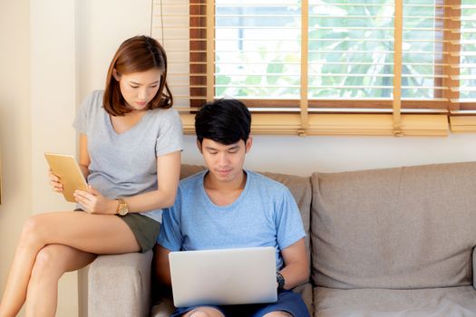 Beautiful young asian couple cheerful freelance working with man using laptop and woman using tablet on couch, family relax and sharing communication together at home, lifestyle concept.