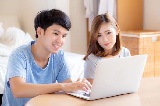 Asian young couple using laptop computer think and searching internet together, man and woman casual smiling work at home with happy and relax, communication and business concept.