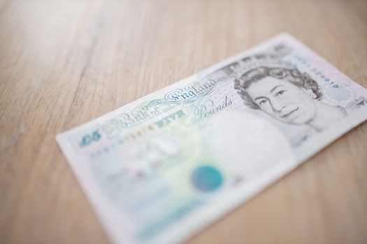 Picture of a Five Pounds Banknote with the face of Queen Elizabeth II, on a Wooden Table