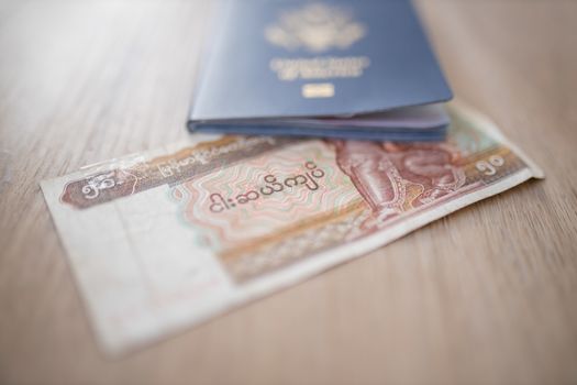 Picture of a blurry United States of America Passport partially on top of a Fifty Burmese Kyats Bill -with the words Central Bank, Fifty Kyas and the number 50 in Burmese-