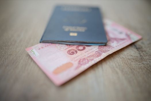 Picture of a 100 Thai Baht Bill -with the number 100 in Thai- Partially Inside a blurry United States of America Passport