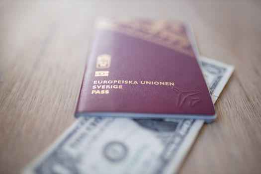 European Union, Sweden Passport with a Two-Dollar Bill Partially Inside of it and both on a Wooden Table