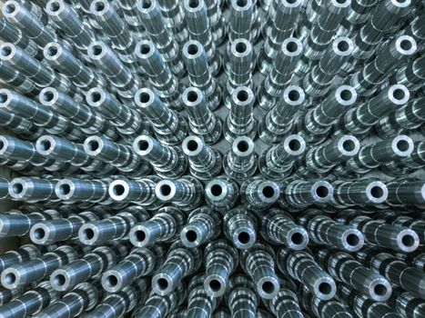 Shiny long steel parts full frame background, clean steel threaded rods after fine cnc turning. Standing vertically in a rows with selective focus in directly above perspective.