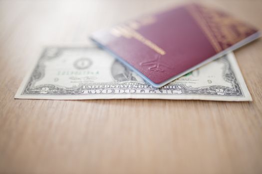 Two Dollars Bill Partially Inside a Blurry Sweden Passport on a Wooden Table