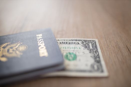 One-Dollar Bill Partially under a United States of America Passport on a Wooden Table