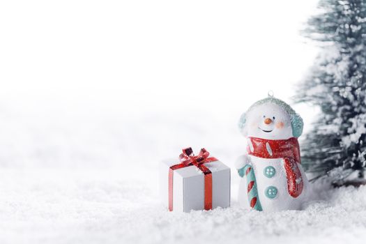 Small cute snowman with gift in fir forest under falling snow