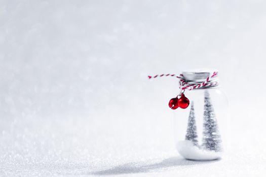 Christmas ornaments of glass jar with striped ribbon , bells and fir trees on snow inside on glitter background