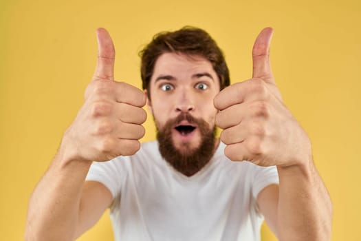 Bearded man emotions fun gesture with hands white t-shirt close-up yellow background. High quality photo