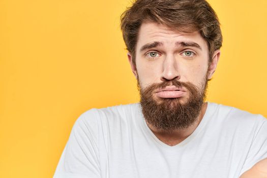 Man in white t-shirt emotions studio gestures with hands displeased facial expression yellow background. High quality photo