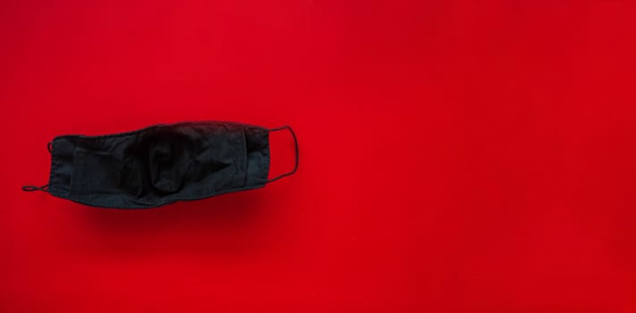A black cloth mask for protection against saliva and dust droplets placed on a red background. During the virus spread heavily
