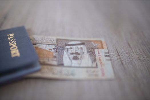 Ten Saudi Riyals Bill -with the words Saudia Arabian Monetary Agency, and the number 10 in Arabic- partially inside an American Passport