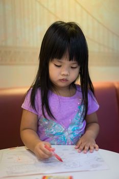 asian little girl sitting and coloring a picture in preschool