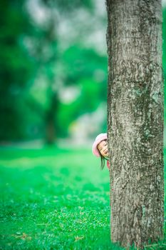 little girl sneaking behind the tree in the forest