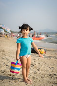 little girl holding a bucket for playing sand on the beach