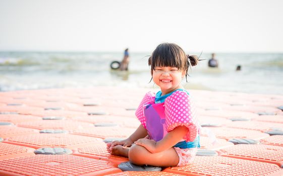 little asian girl wearing inflatable sleeves sitting on the beach