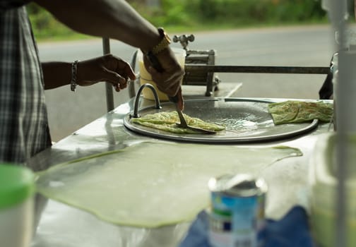 Man's hand fried indian roti on hot pan, roadside