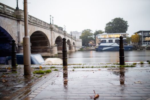 Landscape picture of Chain Posts on a Wet Tile Floor alongside the river, with a bridge as background and under a cloudy sky