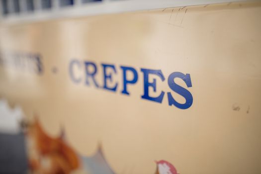 Landscape lateral view of the blue word Crepes on the signboard of an outdoor sweet snacks stand in London, UK