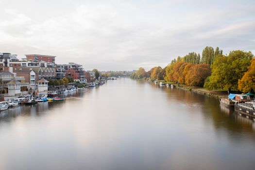 Autumn Colors Landscape Photo Under a Cloudy sky and Over a River that Divides a Town and a Small Forest