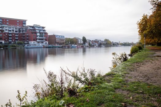 Landscape Picture of a River under a cloudy sky and with Buildings from the Other Side reflecting on the water