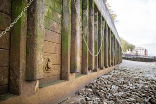 Landscape View of the ground covered in gray rocks, alongside an Orange Concrete Wall Partially Covered by Moss and with chains hanging from it