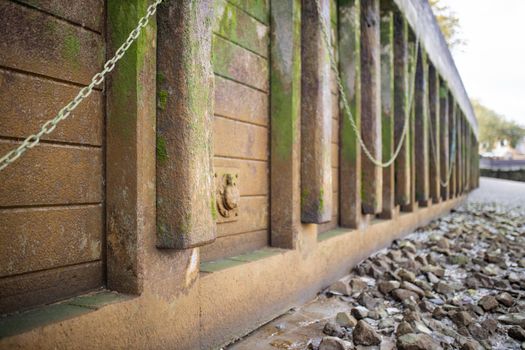 Landscape View of the ground covered in gray rocks, alongside an Orange Concrete Wall Partially Covered by Moss and with chains hanging from it