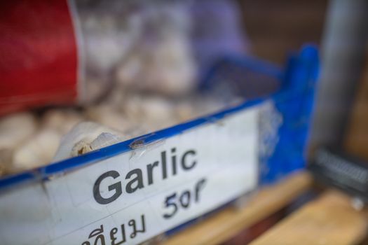 Picture of the word Garlic Written in Thai on Sign on a Blue Plastic Basket Full of blurry Garlic