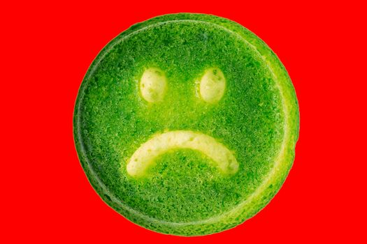 unhappy green face biscuit cookie isolated on red background in flat lay perspective.
