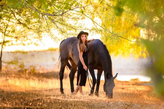 Girl walks in the forest with a horse at sunset