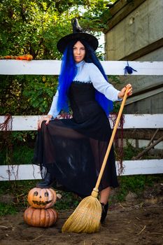 Cute girl in a witch costume with pumpkins and a broom