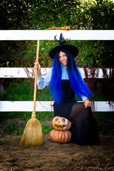 A girl in a witch costume sits on two pumpkins and holds a broom in her hands
