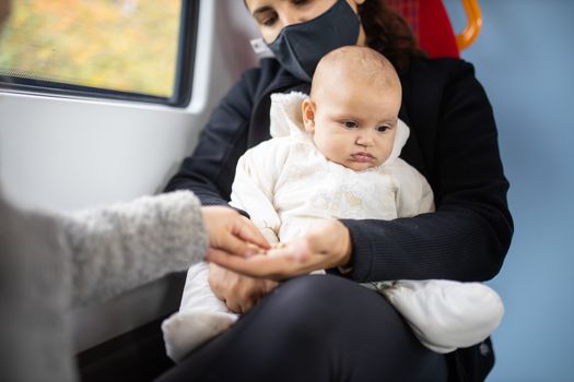 Arm of a little girl in a gray sweater taking pistachios from the hand of her mother who's holding baby sister