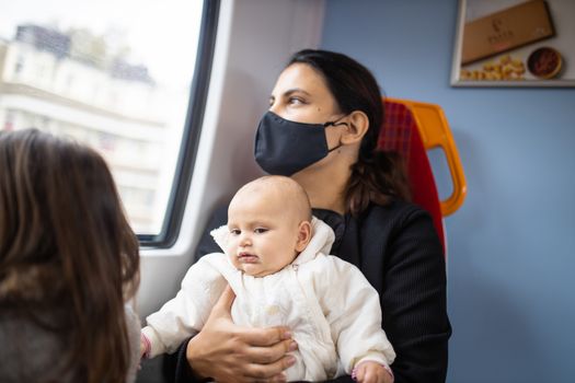 Woman wearing a face mask and looking through the window of a bus as she holds her smiling baby